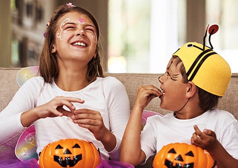 Children in Halloween costumes sitting indoors with pumpkin candy buckets and face paint during a Halloween celebration